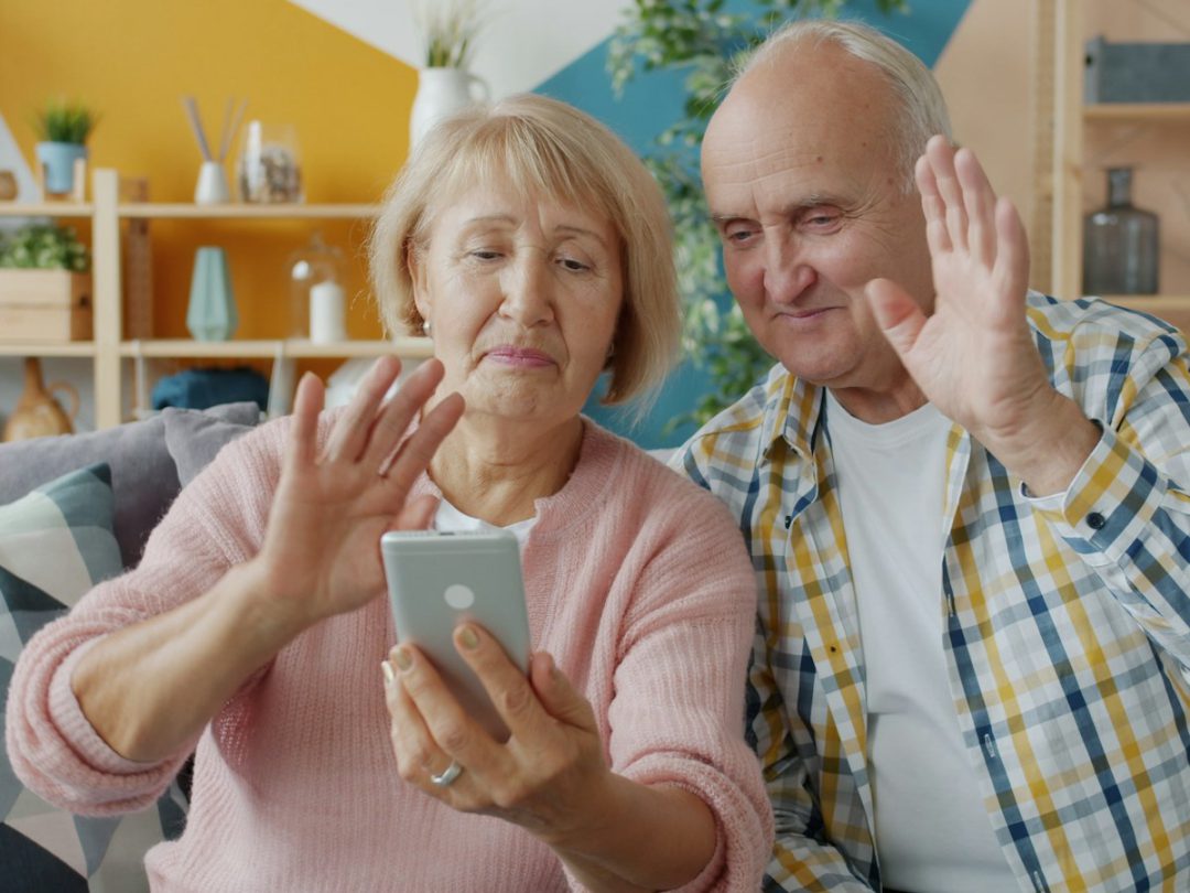 Una pareja de abuelos saludando a la familia por videollamada desde el celular
