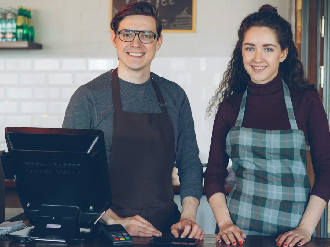 Una pareja sonriendo detrás del mostrador de su local, junto a la caja